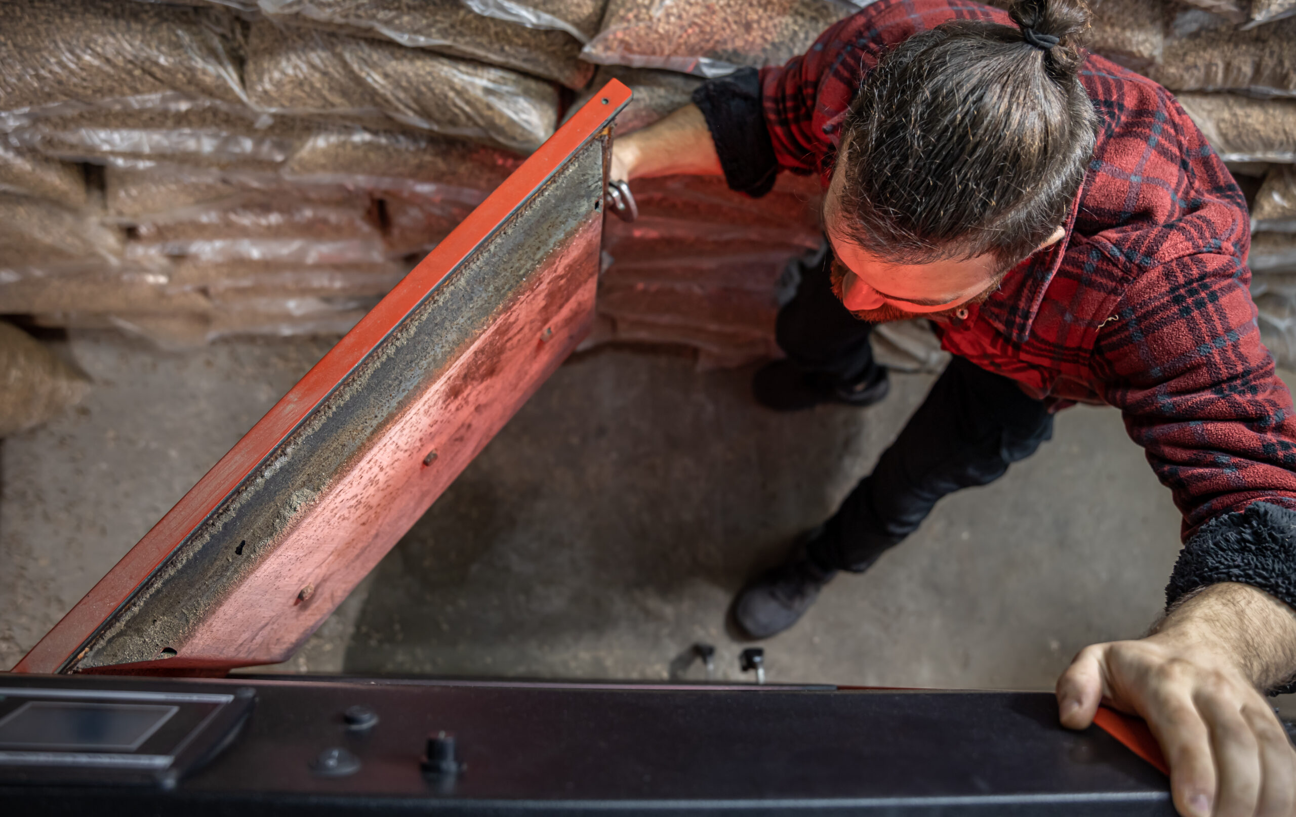 The young man looking into a solid fuel boiler, working with biofuels, economical heating, top view.